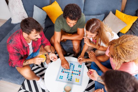 Photo for High angle view of group of cheerful young friends having fun playing ludo board game while spending time together at home - Royalty Free Image