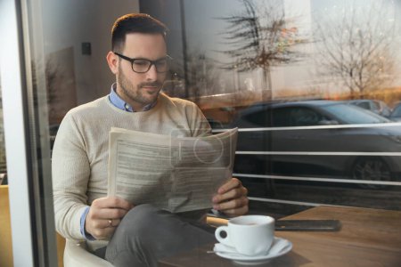 Foto de Hombre guapo sentado en una mesa de restaurante, leyendo periódicos y tomando café - Imagen libre de derechos