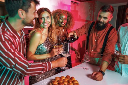 Téléchargez les photos : Groupe d'amis joyeux s'amuser à une fête, ouverture et verser du vin tout en célébrant l'anniversaire ensemble à la maison - en image libre de droit