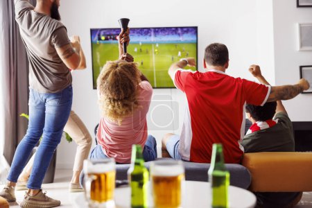 Foto de Grupo de jóvenes amigos divirtiéndose viendo partidos de fútbol en la televisión, bebiendo cerveza y animando; fanáticos del fútbol viendo partidos en casa celebrando después de que su equipo anotara un gol. Concéntrate en el cuerno - Imagen libre de derechos