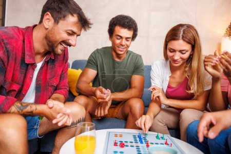 Foto de Grupo de jóvenes amigos alegres que se divierten jugando juego de mesa ludo mientras pasan tiempo juntos en casa - Imagen libre de derechos