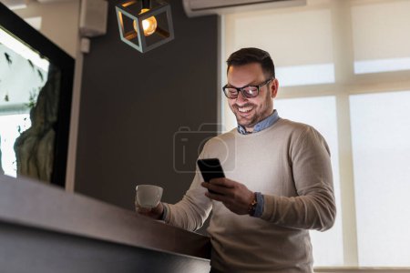 Foto de Hombre guapo de pie junto a un mostrador en el restaurante, navegar por Internet con un teléfono inteligente - Imagen libre de derechos
