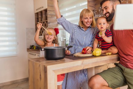 Foto de Hermosa familia feliz divirtiéndose cocinando almuerzo juntos, sentados en el mostrador de la cocina y disfrutando del tiempo libre en casa - Imagen libre de derechos