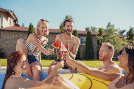 Photo for Group of young friends having fun at summertime swimming pool party, sitting by the pool and eating watermelon popsicles, spending sunny summer day outdoors - Royalty Free Image