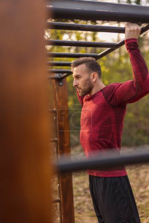 Photo for Men wearing sportswear doing pull ups while having an outdoor workout session in a street workout park - Royalty Free Image