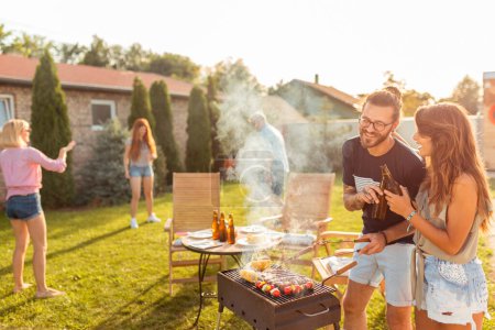 Téléchargez les photos : Groupe de jeunes amis joyeux faisant une fête barbecue arrière-cour, griller de la viande, faire un toast, boire de la bière et s'amuser lors d'une journée d'été ensoleillée - en image libre de droit