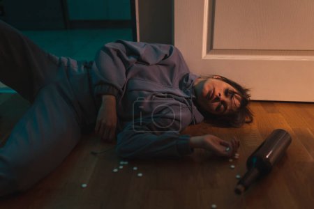 Téléchargez les photos : Femme couchée sur le sol surdosée avec des pilules et de l'alcool ; toxicomane et alcoolique gaspillé sur le sol - en image libre de droit