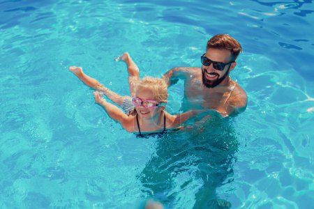 Foto de Vista de ángulo alto de la hermosa niña y su padre divirtiéndose en la piscina en un día de verano soleado caliente, padre enseñando a su hija a nadar - Imagen libre de derechos