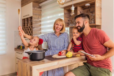 Téléchargez les photos : Belle famille heureuse ayant plaisir à cuisiner le déjeuner ensemble, assis au comptoir de la cuisine et profiter du temps libre à la maison - en image libre de droit