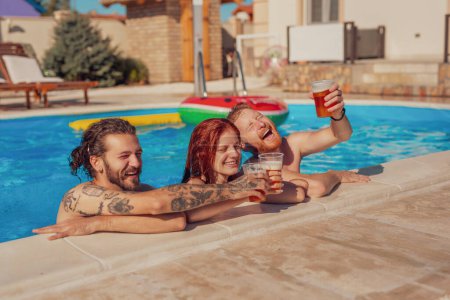 Téléchargez les photos : Groupe de jeunes amis joyeux qui s'amusent à la piscine, penchés sur le bord tout en portant un toast avec des verres de bière, se détendre pendant les vacances d'été - en image libre de droit