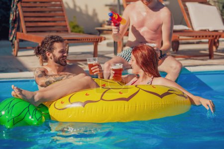 Téléchargez les photos : Groupe d'amis s'amuser et boire de la bière lors d'une chaude journée d'été ensoleillée à la piscine, se détendre pendant les vacances d'été - en image libre de droit