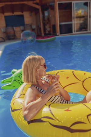 Photo for Attractive young woman wearing swimsuit drinking cocktail while floating on pool raft, enjoying sunny summer day at the swimming pool - Royalty Free Image
