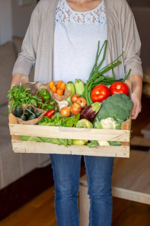 Téléchargez les photos : Femme tenant une caisse en bois nouvellement livrée remplie de divers légumes biologiques frais - en image libre de droit