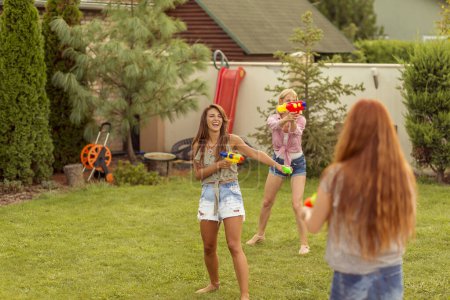 Foto de Grupo de jóvenes amigos que se divierten pasando el día de verano al aire libre, jugando con pistolas de agua, salpicándose agua, corriendo y persiguiéndose mutuamente - Imagen libre de derechos