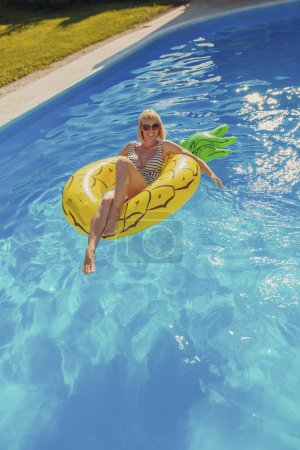 Photo for Attractive young woman wearing swimsuit floating on swimming float, enjoying sunny summer day at the swimming pool, relaxing while on summer vacation - Royalty Free Image