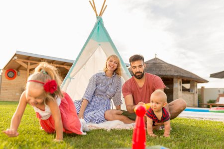 Photo for Happy family having fun spending sunny summer day camping in the backyard, parents playing bowling with their little children, throwing a ball and knocking the pins down - Royalty Free Image