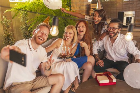 Foto de Grupo de jóvenes amigos alegres divirtiéndose tomando selfies con pastel y regalos en una fiesta de cumpleaños - Imagen libre de derechos