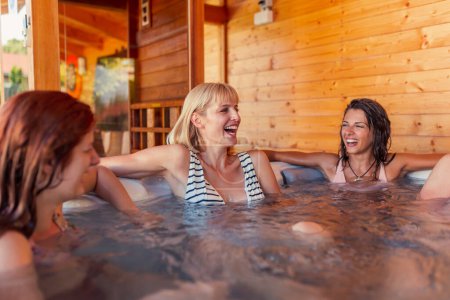 Foto de Grupo de mujeres jóvenes y alegres que se relajan en una bañera de hidromasaje del centro de spa del hotel, divirtiéndose mientras están de vacaciones - Imagen libre de derechos