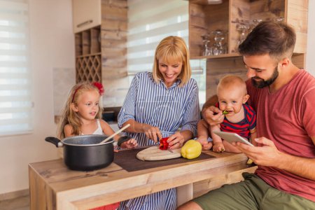 Photo for Beautiful happy family having fun cooking lunch together, sitting at kitchen counter and enjoying leisure time at home - Royalty Free Image