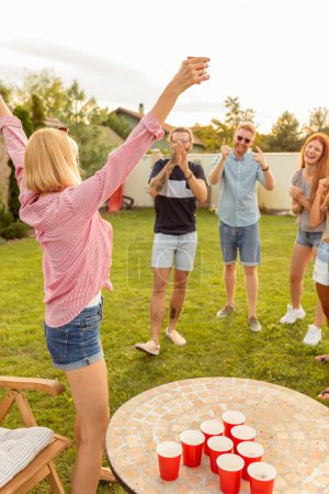 Photo for Group of cheerful young friends having fun while playing beer pong at backyard summertime party, cheering for each other - Royalty Free Image
