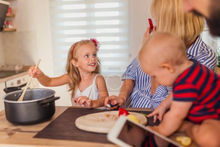 Photo for Cheerful young family having fun cooking lunch together, sitting at kitchen counter and enjoying leisure time at home - Royalty Free Image