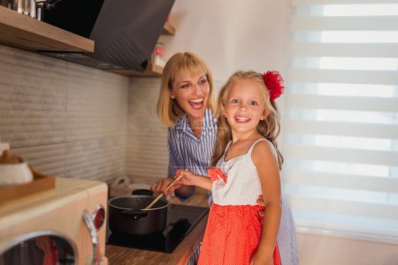Photo for Beautiful mother and daughter having fun cooking lunch togehter in the kitchen - Royalty Free Image