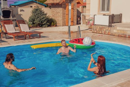 Grupo de amigos divirtiéndose al aire libre en un día caluroso y soleado de verano, jugando voleibol en la piscina, relajándose durante unas vacaciones de verano