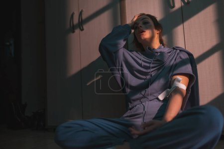 Foto de Mujer sentada en el suelo en la oscuridad después de inyectarse heroína; drogadicta tras la inyección intravenosa de heroína desperdiciada en el suelo - Imagen libre de derechos