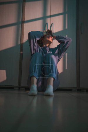 Photo for Desperate young woman sitting on the floor in the dark holding head in hands, crying and screaming - Royalty Free Image