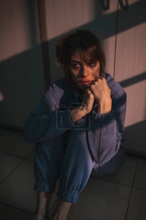 Mujer con problemas de salud mental sentada en el suelo en la oscuridad con maquillaje manchado después de llorar, molesto y asustado
