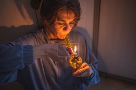 Foto de Mujer joven deprimida sentada en el suelo en la oscuridad, fumando marihuana usando pipa; mujer vapeando marihuana con pipa - Imagen libre de derechos