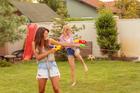 Téléchargez les photos : Groupe de jeunes amis s'amuser passer la journée d'été à l'extérieur, jouer avec des pistolets à éjaculation féminine, éclabousser de l'eau les uns sur les autres, courir et courir après les autres - en image libre de droit