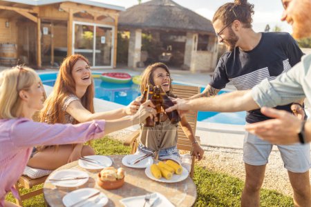 Téléchargez les photos : Groupe de personnes qui s'amusent à la fête barbecue au bord de la piscine, faire un toast avec des bouteilles de bière et profiter des journées ensoleillées d'été en plein air - en image libre de droit