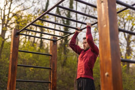 Photo for Men in sportswear doing pull ups while working out outdoors in a street workout park - Royalty Free Image