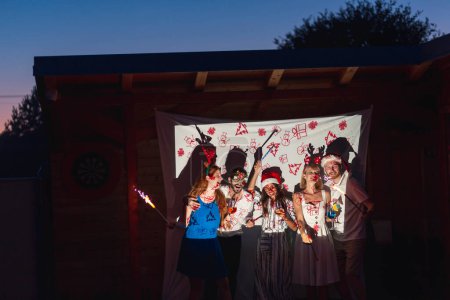 Téléchargez les photos : Groupe d'amis s'amusant à la fête de la Saint-Sylvestre, sifflements de fête et saluant avec étincelles au compte à rebours de minuit - en image libre de droit