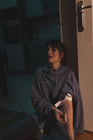Téléchargez les photos : Femme assise par terre dans le noir tirant avec de l'héroïne ; toxicomane s'injectant de l'héroïne par voie intraveineuse ; concept de toxicomanie et de toxicomanie - en image libre de droit