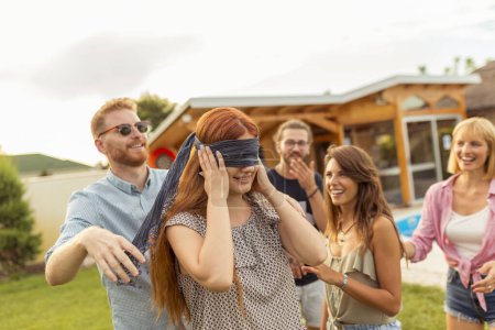 Téléchargez les photos : Groupe de jeunes amis joyeux s'amusant à la fête en plein air au bord de la piscine en été, jouant le buff de l'aveugle, courant et se poursuivant sur la pelouse arrière-cour - en image libre de droit