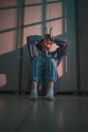 Photo for Desperate young woman sitting on the floor in the dark crying and screaming - Royalty Free Image