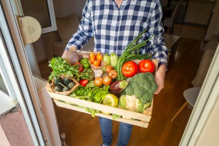 Photo for Woman holding newly delivered wooden crate with rich selection of fresh organic vegetables - Royalty Free Image