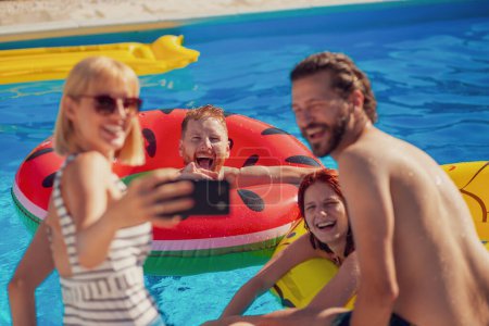 Photo for Two beautiful young couples having fun at the swimming pool on a sunny summer day, taking a selfie using smart phone, relaxing and sunbathing by the pool - Royalty Free Image