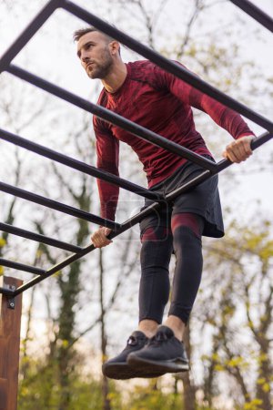 Photo for Active man doing pullups while exercising outdoors in a street workout park - Royalty Free Image
