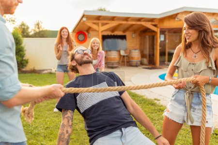 Gruppe fröhlicher junger Freunde, die sich bei der sommerlichen Outdoor-Party am Schwimmbad vergnügen, am Limbo-Tanzwettbewerb teilnehmen und beim Tanzen unter dem Seil hindurchgehen