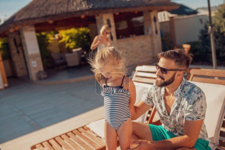 Téléchargez les photos : Jeune père et petite fille assis sur un transat au bord de la piscine, se détendre et jouer à l'extérieur pendant les vacances d'été - en image libre de droit