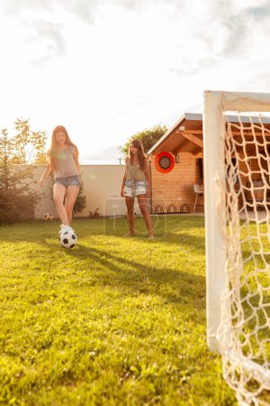 Photo for Group of young friends having fun while playing football on the backyard lawn on sunny summer day; young business team on team building trip, participating in mini football competition - Royalty Free Image