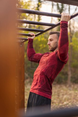 Photo for Men wearing sportswear doing pull ups while having an outdoor workout session in a street workout park - Royalty Free Image