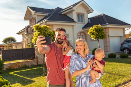 Téléchargez les photos : Belle famille heureuse s'amuser à prendre selfie en utilisant un téléphone intelligent devant leur nouvelle maison - en image libre de droit