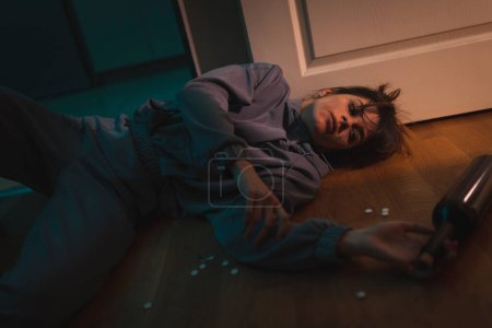 Téléchargez les photos : Femme ivre couchée sur le sol s'est évanouie avec des pilules et une bouteille de vin autour d'elle ; toxicomane et alcoolique gaspillé sur le sol - en image libre de droit
