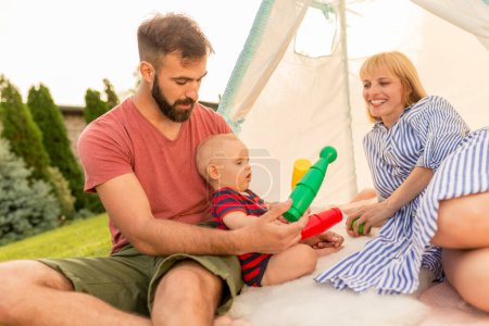 Foto de Los padres jóvenes se divierten acampando en el patio trasero y jugando con su pequeño bebé en un día soleado de verano - Imagen libre de derechos