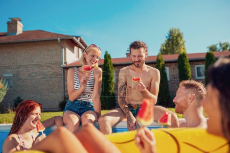 Photo for Group of young friends having fun at summertime swimming pool party, sitting by the pool and eating watermelon popsicles - Royalty Free Image