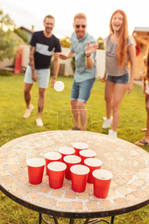 Téléchargez les photos : Groupe de jeunes amis joyeux s'amuser tout en jouant au bière pong à la fête d'été arrière-cour, acclamant l'un pour l'autre - en image libre de droit